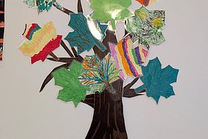 Wanddekoration aus Papier mit einem braunen Baumstamm und Ästen, an denen bunte, unterschiedlich gemusterte Papierblätter in verschiedenen Formen befestigt sind