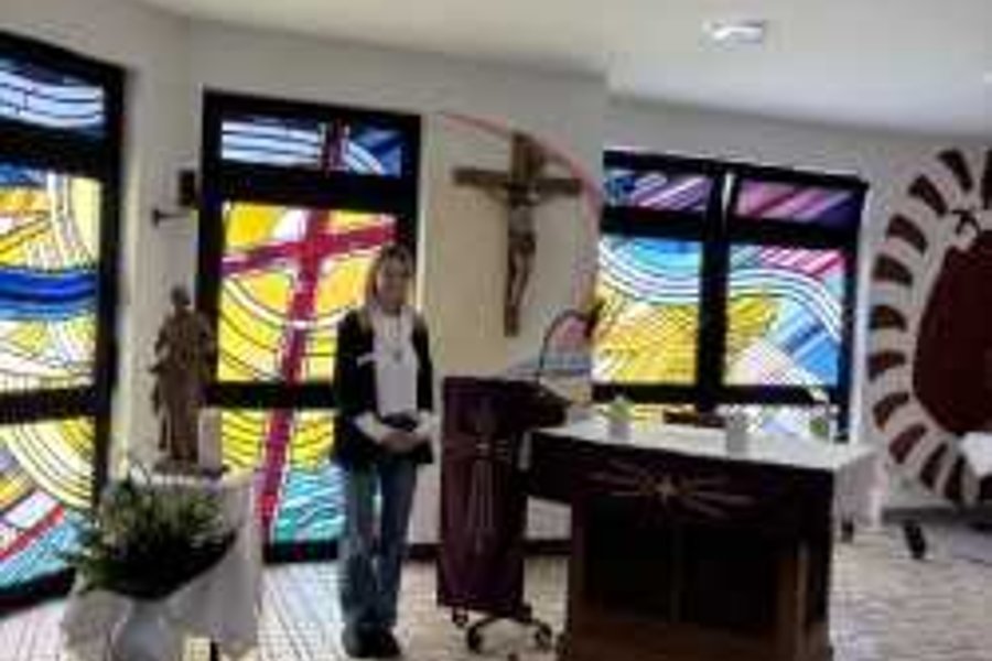Person steht in einem Raum mit bunten Glasfenstern, einem Altar und einem großen Kreuz an der Wand
