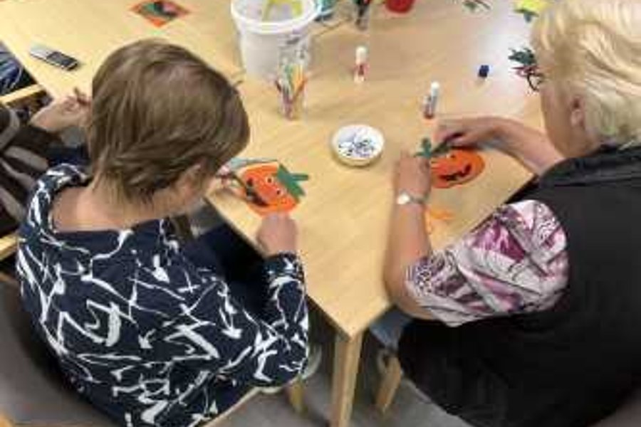 Zwei ältere Frauen sitzen an einem Tisch und bemalen Kürbisse mit Pinseln
